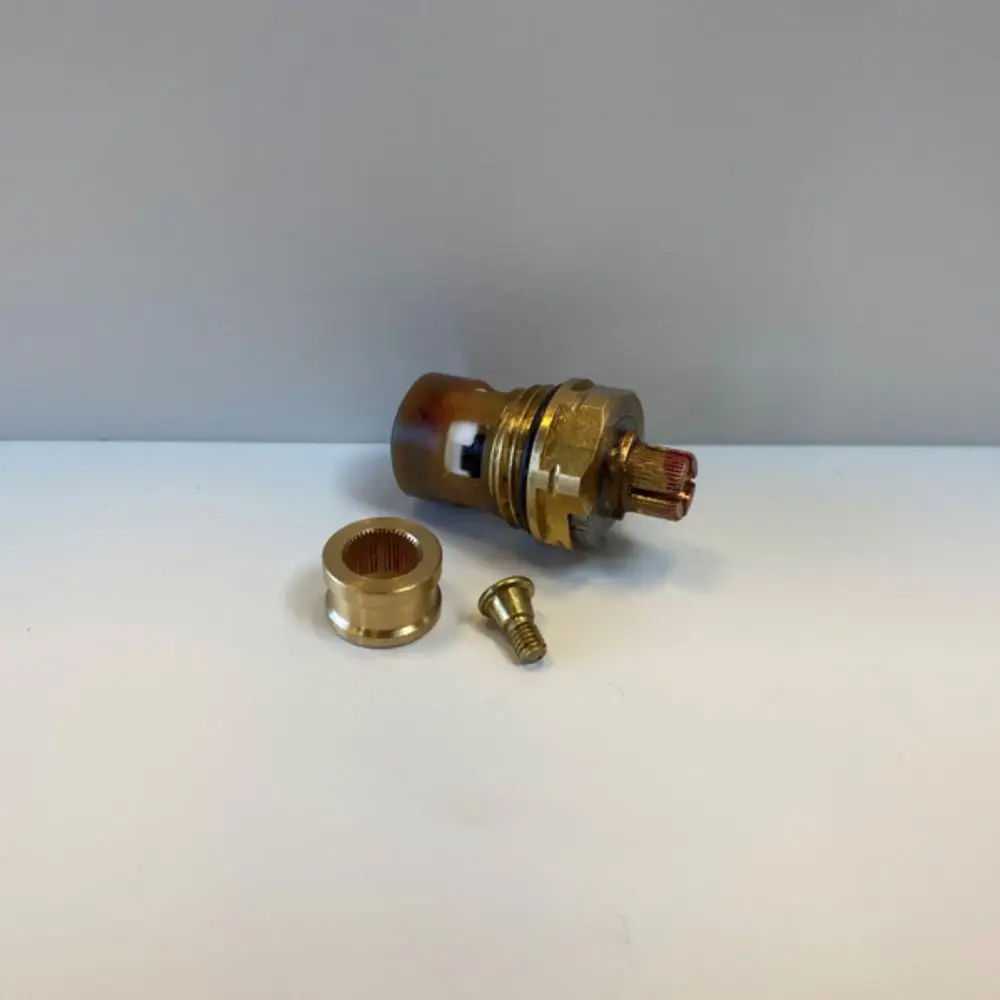 Ideal Standard Metallbauteile, bestehend aus einem zylindrischen Hauptteil mit Gewinde, einer Zwischenhülse und einer Schraube, auf hellem Hintergrund.
